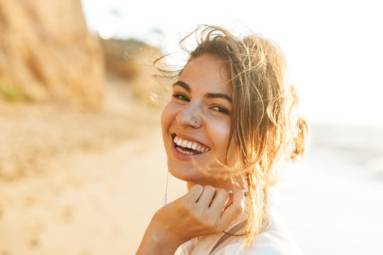 Image of positive brunette girl 20s laughing, while walking by seaside