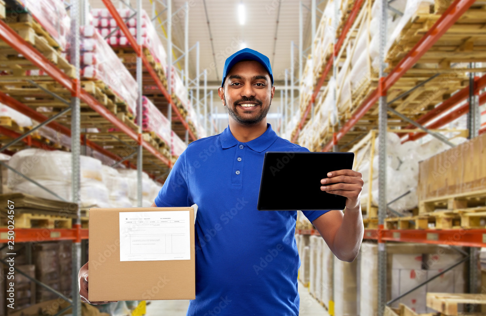 Wall mural mail service, technology and shipment concept - happy indian delivery man or warehouse worker with parcel box and tablet computer in blue uniform over goods background