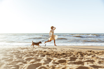 Fototapeta na wymiar Image of beautiful woman in straw hat, running with her brown dog along the coast