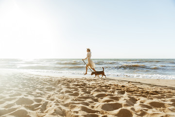 Fototapeta na wymiar Image of happy woman in straw hat, running with her brown dog along the coast