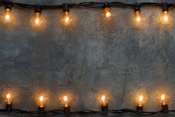 Garlands of glowing warm glass lamps on grunge wall with copy space
