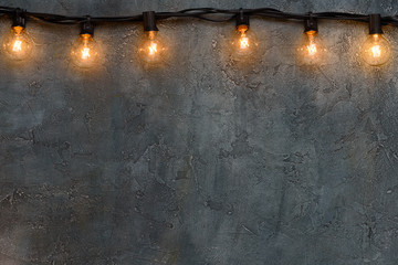 Garland of warm glowing edison glass lamps on rustic wall border