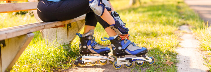 Woman is going rollerblading. Sitting on a bench in a park and putting on inline skates. Close up....