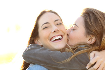 Woman kissing her happy friend with perfect smile