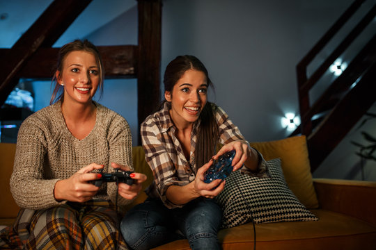 Two female best friends sitting at home on pleasant evening and playing games on console.They challenge each other to win.