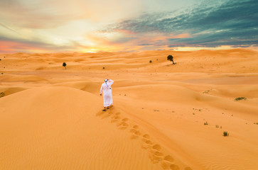 Fototapeta na wymiar Arabic man with traditional emirates clothes in the desert, sunset.