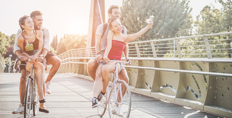 Happy friends taking selfie photo with smartphone on bicycle outdoor - Main focus on right couple