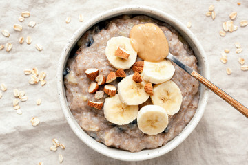 Bowl of oatmeal porridge with banana and peanut butter over linen background. Top view. Healthy vegan breakfast - Powered by Adobe