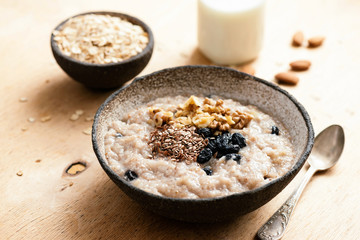 Oatmeal porridge with raisin and seeds in bowl on wooden table. Tasty healthy breakfast. Morning vegan meal - obrazy, fototapety, plakaty