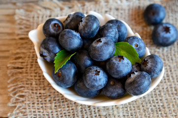 Freshly picked organic blueberries in a white bowl on a burlap cloth background. Blueberry. Bilberries.Healthy eating,vegan food or diet concept.Selective focus.