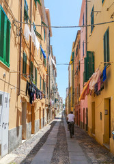 Fototapeta na wymiar Alghero, Sardinia / Italy - June 18, 2015: Hanging clothes in a narrow street at the old city centre and a man riding a bicycle