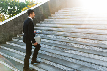 Handsome young businessman walking outdoors at the street holding clipboard.