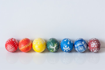 Rainbow line of easter eggs on white background with reflection. Easter holiday concept. Still life with traditional Marguciai, decorated Easter eggs.  Copy space.