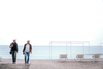 Two men photographer friends with camera and smartphone in hand are walk at the beach during their holidays. work and travel, enjoy the moment, freelancers enjoy life, space for te?t