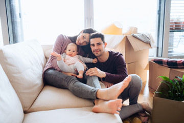 A portrait of young couple with a baby and cardboard boxes moving in a new home.