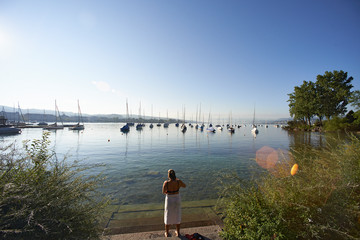 Caucasian woman wrapped in a towel standing on the shore of Lake Zuricu after an early morning swim in the lake