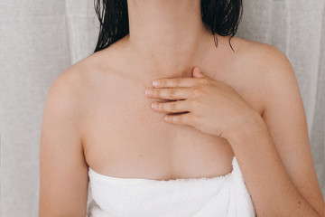 Relaxed sexy woman in white towel applying moisturizing cream on neck in bathroom, closeup. Skin...