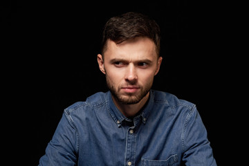 Man in denim shirt looking sideways with doubtful expression