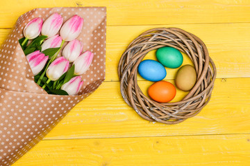 Spring vibes. Colorful eggs and bouquet fresh tulip flowers on yellow background top view. Spring holiday. Tradition celebrate easter. Happy easter season. Easter is coming. Collecting easter eggs