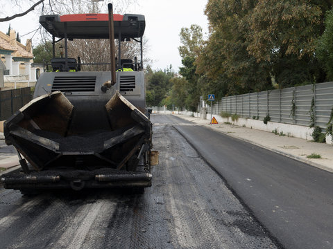 M&aacute;quina moderna pesada de asfaltar que extiende y presiona el asfalto caliente. M&aacute;quina de reparaci&oacute;n de carreteras. Reparaci&oacute;n de carretera en ciudad moderna, antes de pasar otra m&aacute;quina apisonadora.