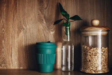 Bulk store shopping. Glass jar with cereals, reusable coffee cup and bamboo leaves on wooden shelf. Zero waste concept, sustainable lifestyle. Ban single use plastic.