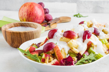 Waldorf salad with apples, celery, grapes, walnuts and arugula on white plate