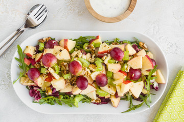Waldorf salad with apples, celery, grapes, walnuts and arugula on white plate, top view