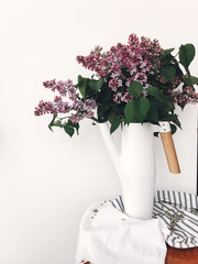 Beautiful lilac flowers in white stylish watering can on white background indoors. Modern decor...