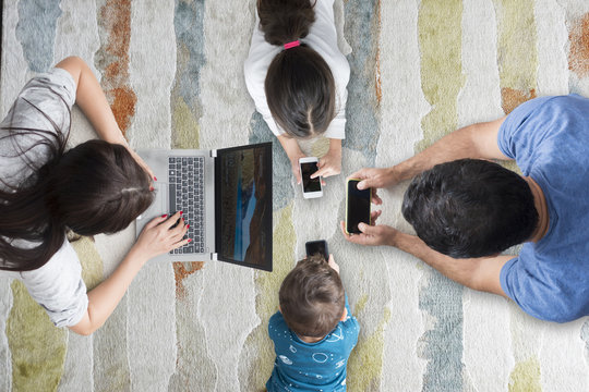 Four members family browsing smartphones and laptop on living room, internet addiction concept