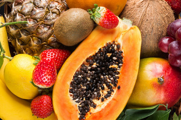 Heap of raw organic tropical and seasonal summer fruits berries halved papaya, coconut mango kiwi bananas pineapple strawberries citrus in sunlight. Healthy vegan lifestyle vitamins detox