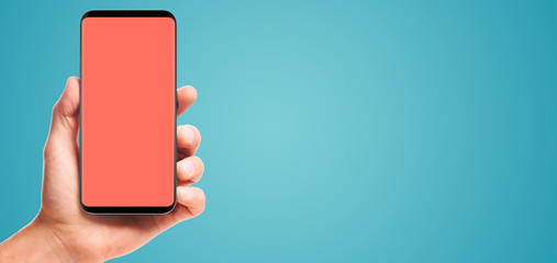 male hand holding bezel-less smartphone with blank living coral screen, isolated on blue background . Screen is cut out with path
