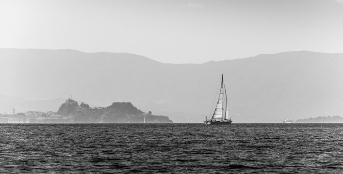 Black and white photo of sailing boat. Old fortress of Corfu in the background