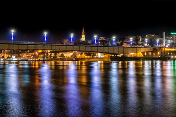 Fototapeta na wymiar Belgrade, Serbia - February 10, 2019: A panorama of Belgrade seen from the banks of the Sava River by night with reflection. View of the Brankov Bridge. 