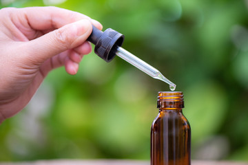 hand holding pipette with oil over bottle on blurred background