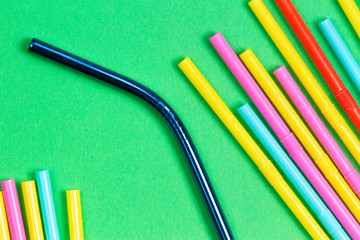 Stainless steel reusable drinking straw with plastic straws on green background