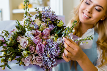 smiling female florist arranging bouquet with lilac and roses in flower shop