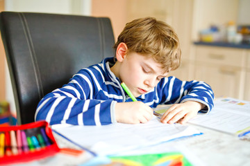 Portrait of frustrated crying sad school kid boy at home making homework. Little child writing with colorful pencils, indoors. Elementary school and education, heavy burden at school