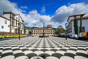 Beautiful cityscape of the townsquare Praca do Municipio in Funchal, Madeira, with the Church of St. John the Evangelist and the city hall, on a summer day with blue sky and clouds - obrazy, fototapety, plakaty