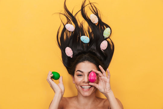 Pleased happy young woman lies isolated on yellow background over easter eggs.