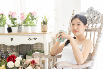 Portrait Asian woman relaxing on wooden chair with coffee at home