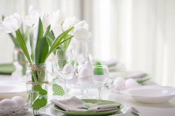 Decor and table setting of the Easter table with white tulips and dishes of green and white color. Easter decor in the form of Easter bunnies  green color with white polka dots.