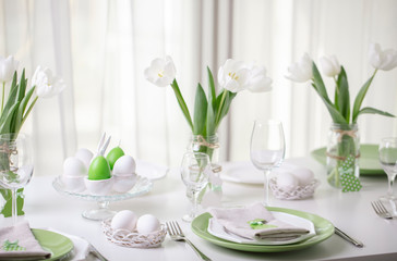 Decor and table setting of the Easter table with white tulips and dishes of green and white color. Easter decor in the form of Easter bunnies  green color with white polka dots.