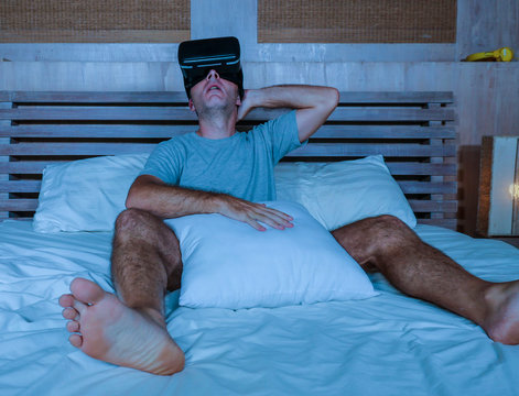 young excited and aroused man at home wearing 3d virtual realty goggles having fun on bed playing alone with internet cyber sex VR simulator in sexual illusion and desire