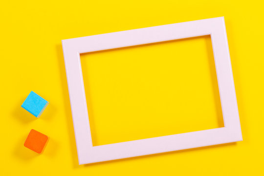 Baby kids toys background with empty frame and wooden cubes on yellow background