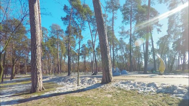 Time lapse panorama, park in a pine forest with a playground in early spring, on the lawn there are pockets of unmelted snow, clear weather
