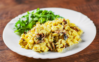 scrambled eggs with mushrooms and arugula salad in white plate on wooden table background