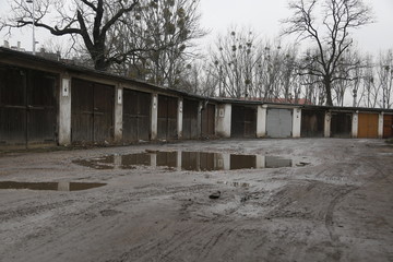 Old, neglected, ruined garages. Muddy, holey, uneven road with puddles. Winter, autumn landscape in the city. Wrocław, Wroclaw, Breslau. Lower Silesia, Dolny Śląsk. Polska, Poland, Polen