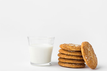 Stack of freshly home baked oatmeal and coconut cookies and glass of milk on white kitchen table wall background. Australian anzac biscuits recipe. Clean contemporary minimalist style. Copy space
