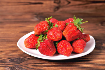 red large strawberries in a white plate on a natural brown background close-up