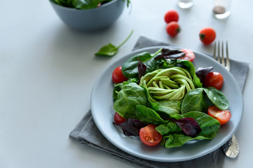 Salad mix with avocado, spinach, tomatoes and beet leaves on gray wooden background. Vegetarian food concept. Selective focus.